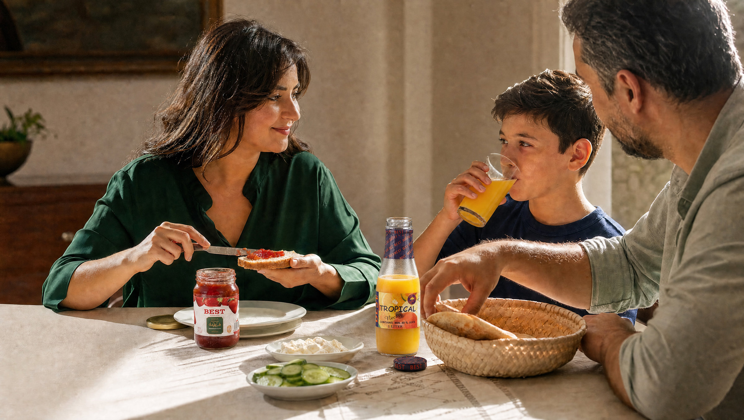 A mother spreads BEST strawberry jam at a sunlit family breakfast while her son drinks mango nectar